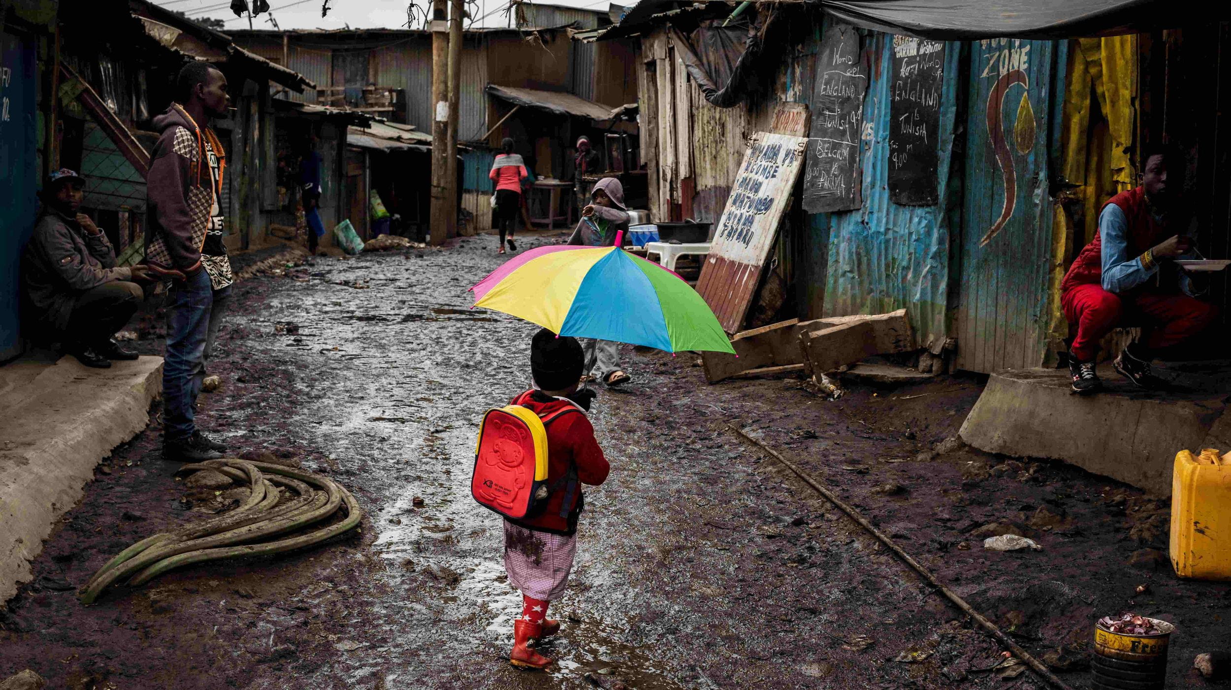 Ein Mädchen läuft mit einem bunten Regenschirm durch eine schlammige Straße in einem Slum in Nairobi. (Quelle: Lars Heidrich)