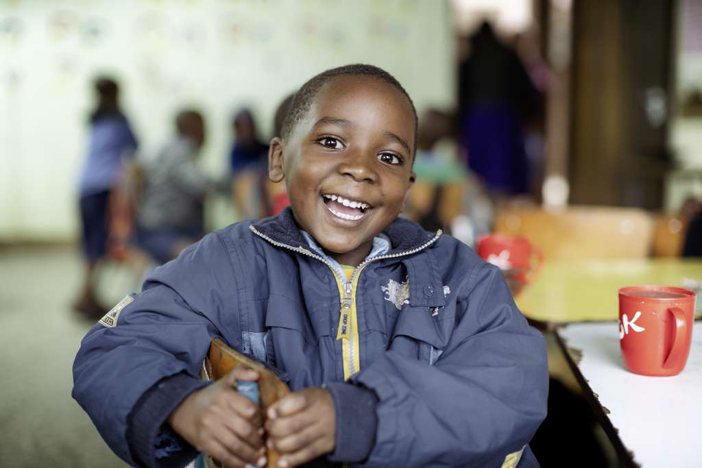 Ein Junge aus Kenia sitzt lachend an einem Tisch. (Quelle: Lars Heidrich)